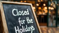 Closed for holidays chalkboard sign at restaurant entrance with warm bokeh lights creating festive atmosphere for seasonal business closure announcement.