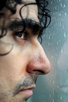 Close-up profile view of a young Mediterranean man with dark curly hair looking through rainy window glass, expressing contemplation and melancholy.