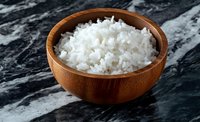 Cooked white rice in wooden bowl on dark marble surface, ready for meal preparation and cooking projects.