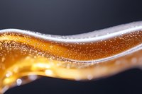 Golden liquid wave with bubbles and foam creates dynamic flowing pattern against dark background, macro photography for beverage advertising.