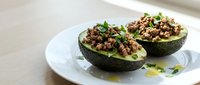Halved avocado filled with seasoned ground meat and chickpeas, garnished with fresh herbs, served on white plate for healthy lunch or dinner meal preparation.