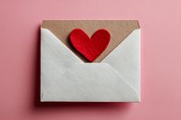 Open white envelope with red felt heart peeking out on pink background, symbolizing love message or romantic correspondence.