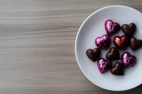 Heart shaped chocolate candies and pink foil wrapped sweets on white ceramic plate against wooden table background, romantic holiday confectionery composition.