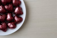 Red foil wrapped chocolate hearts in white bowl on wooden table for Valentine's Day celebration, romance, love gifts and sweet treats.