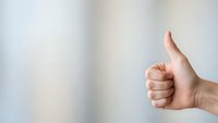 Hand showing thumbs up gesture against neutral background expressing approval and positive feedback for business communication.