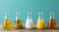 Laboratory glassware with colorful chemical solutions on wooden table against turquoise background for scientific research and experimentation.