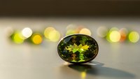 Green peridot gemstone with faceted cut displaying brilliant sparkle and light reflections on neutral surface with colorful bokeh lights background.