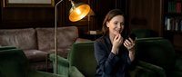 Young professional woman relaxing on green velvet sofa using smartphone in cozy living room with warm lighting for lifestyle and technology concepts.