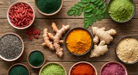 Colorful superfood powders and supplements arranged in wooden bowls on rustic table. Turmeric, spirulina, goji berries, chia seeds, ginger root, moringa.