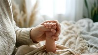 Tender moment as a parent gently holds a newborn baby's tiny foot, capturing the bond of love and care in a soft, cozy home setting.