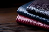 Genuine leather wallets in navy blue and burgundy red stacked on dark wooden surface showing detailed grain texture and premium quality material.