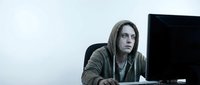Young Caucasian male programmer in hoodie working late at computer desk in modern office environment for technology and coding projects.