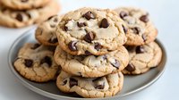 Fresh baked chocolate chip cookies stacked on gray ceramic plate, showing gooey melted chips and golden brown edges, close up view of homemade dessert treats.