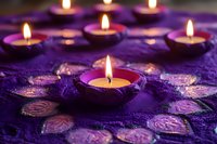 Lit tea lights arranged on purple fabric with decorative patterns, creating warm ambient lighting for meditation, relaxation, spiritual ceremonies, or home decor settings.