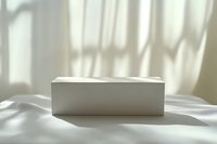 White rectangular box on surface with natural window light and shadow patterns casting across neutral background.