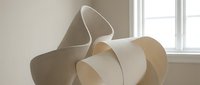 Abstract sculptural paper forms with flowing curves and organic shapes creating artistic composition in minimalist interior space with natural lighting.
