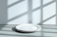 Empty white ceramic plates on light gray surface with window shadow overlay creating minimalist composition and geometric pattern. Natural lighting.