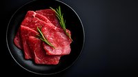 Fresh raw beef steaks with rosemary sprigs arranged on black plate against dark background, dramatic food photography highlighting meat texture and quality.