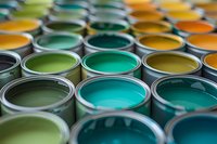 Open paint cans showing vibrant green, turquoise, and yellow colors arranged in rows, creating depth of field effect with selective focus for interior design projects.