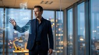 Confident businessman presenting data analytics on transparent screen in modern office with city skyline view at evening.