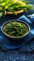 Fresh green tea leaves in traditional woven basket on dark blue textile background with natural lighting for culinary and wellness concepts.