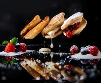 Fresh crepes with dripping cream and berries on dark background, dramatic food photography with reflection and floating composition.