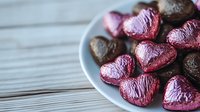 Pink and dark chocolate heart shaped candies on white plate against rustic wooden background, romantic holiday confectionery arrangement for Valentine's Day celebration.