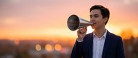 Young Caucasian businessman in suit speaking through vintage megaphone at sunset, urban bokeh background, announcing leadership message.