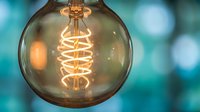 Vintage Edison light bulb with glowing spiral filament against blurred turquoise background for modern interior design and creative lighting concepts.