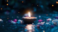 Glowing candle flame surrounded by scattered rose petals in dark blue atmospheric setting with bokeh lights creating peaceful spa or meditation ambiance.