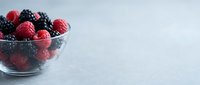 Fresh raspberries and blackberries in glass bowl on white textured surface, ideal for food and beverage design projects.