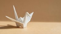 White origami crane on warm beige background with copy space, symbolizing peace, hope, and Japanese paper folding art for cards and decor.