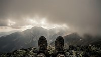 Hiker boots resting on rocky summit overlooking misty mountain peaks under dramatic cloudy sky. Adventure travel and outdoor exploration concept.