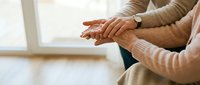 Elderly couple holding hands together in warm sweater clothing showing love support and care in bright indoor setting for relationship concepts.