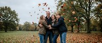 Family of four enjoying autumn outdoors, tossing falling leaves in park setting. Multigenerational bonding moment perfect for lifestyle, seasonal, and family-themed marketing campaigns.