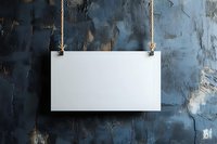 Blank white rectangular sign hanging on rope against dark textured wall with peeling paint and dramatic lighting, mockup for advertising and branding.