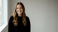 Young professional woman with long wavy hair smiling confidently in black sweater against neutral background for business and lifestyle content.