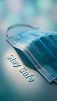Blue surgical face mask with Stay Safe text on teal surface, health protection and pandemic safety concept for medical campaigns.