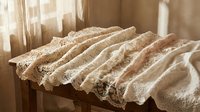 Vintage lace fabric draped elegantly on wooden surface in soft natural sunlight creating romantic shabby chic atmosphere for wedding decor projects.