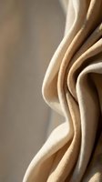 Closeup of folded beige linen fabric with soft natural lighting, showcasing texture and draping for textile, fashion, and interior design projects.