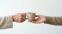 Two hands passing a ceramic mug on white background, symbolizing care, sharing, and connection between generations.