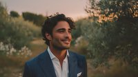 Young handsome Mediterranean businessman in elegant navy suit smiling confidently outdoors during golden hour sunset with natural landscape background.
