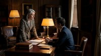 Two mature professionals engaged in serious discussion at wooden desk in elegant office setting with warm lighting and classic furnishings. Suitable for corporate, business negotiation, leadership and professional communication concepts.
