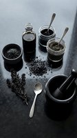 Black activated charcoal powder and liquid in glass jars with spoons on dark surface for detox skincare and wellness treatments.