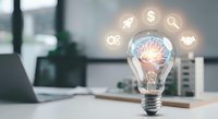 Light bulb with glowing brain inside surrounded by business icons on office desk representing innovation, creativity and entrepreneurship concepts.