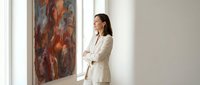 Professional businesswoman in white suit admiring abstract artwork in modern gallery space, perfect for corporate and cultural marketing materials.
