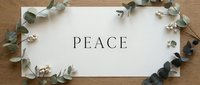 White card with the word Peace surrounded by eucalyptus branches and white berries on a wooden surface, evoking calm and harmony.