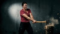 Strong man in red shirt swinging sledgehammer with wood chips flying in dramatic lighting for fitness and strength training concepts.