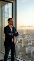 Confident Caucasian businessman in navy suit standing by office window overlooking city skyline at sunset, arms crossed, contemplating future business growth.