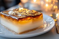 Layered dessert with creamy white base and glossy caramel topping on white plate, elegant dining setting with warm bokeh lights, suitable for restaurant menus and food blogs.